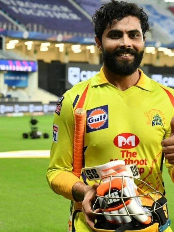 運動 桌布 壁紙 — 一位微笑的板球運動員身穿黃色 Chennai Super Kings 球衣，在體育場上手持球棒和頭盔。