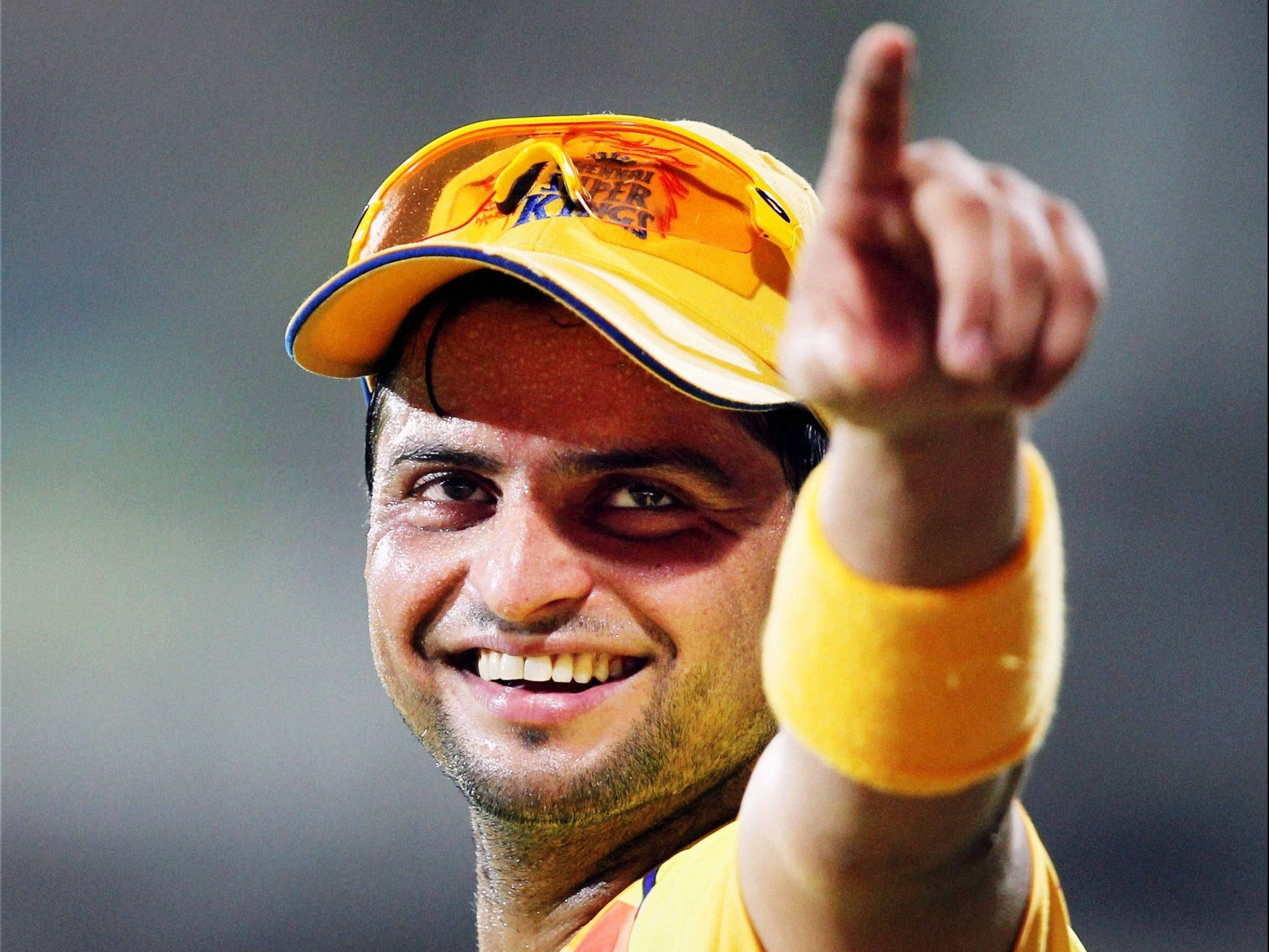 Chennai Super Kings 桌布 壁紙 — 一位微笑的板球運動員身穿黃色裝備，在體育場燈光下帶著喜悅的表情向上指。
