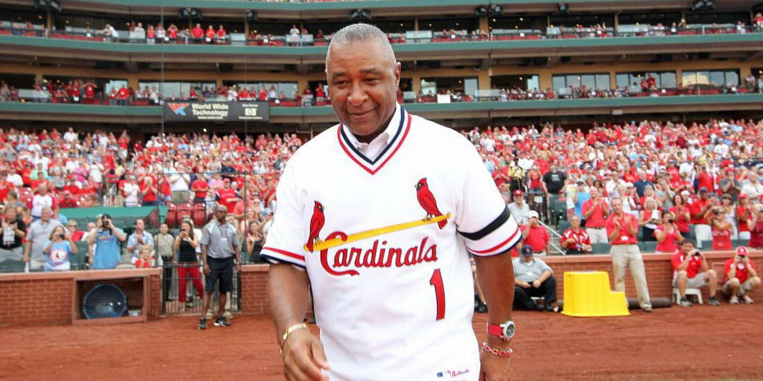 Ozzie Smith 桌布 壁紙 — 一位微笑的棒球傳奇人物身穿白色紅雀隊球衣，走過陽光普照的球場，身穿紅衣的球迷為他歡呼。