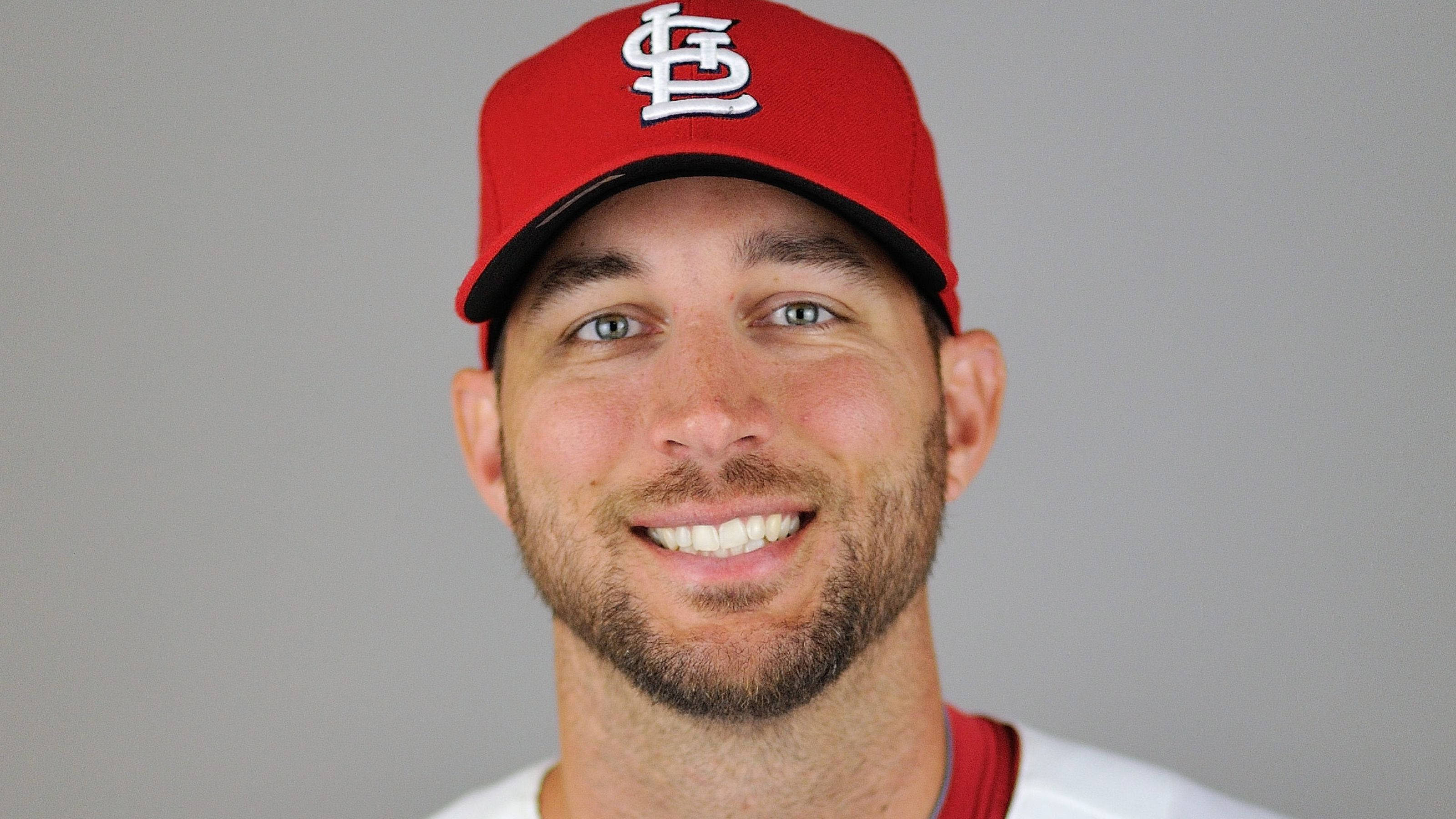 Adam Wainwright 桌布 壁紙 — 一位微笑的棒球運動員，戴著紅色聖路易紅雀隊帽子，背景為純灰色。