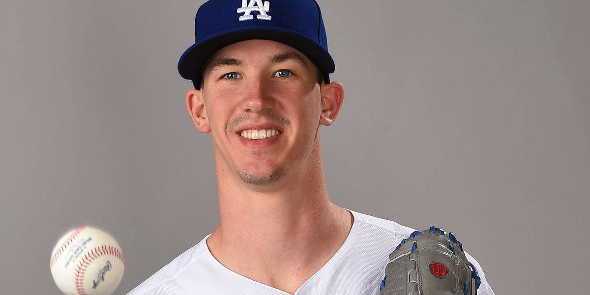 walker buehler 桌布 壁紙 — 一位微笑的棒球運動員戴著道奇隊帽子和手套，在灰色攝影棚背景前與棒球合影。