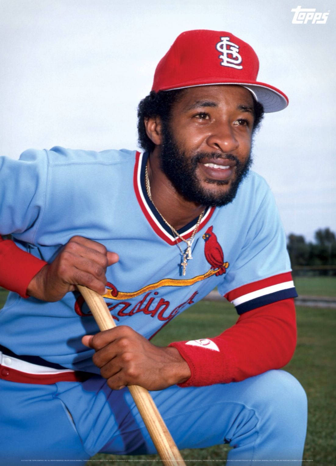 Ozzie Smith 桌布 壁紙 — 一位微笑的棒球運動員穿著淺藍色和紅色的紅雀隊制服，蹲著拿著球棒，背景是草地。