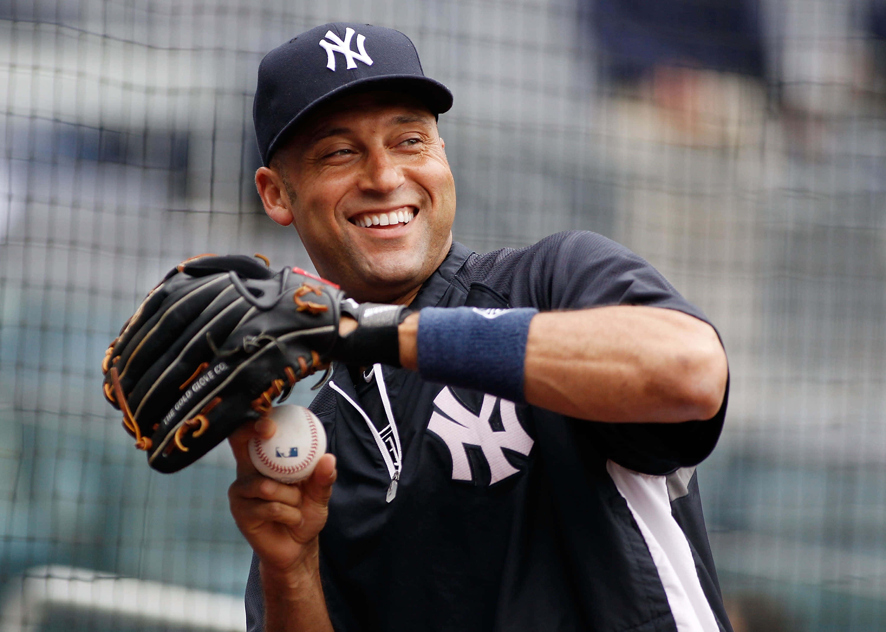 MLB Players 桌布 壁紙 — 一位微笑的棒球運動員穿著紐約洋基隊制服，拿著棒球和手套，在網附近擺姿勢。
