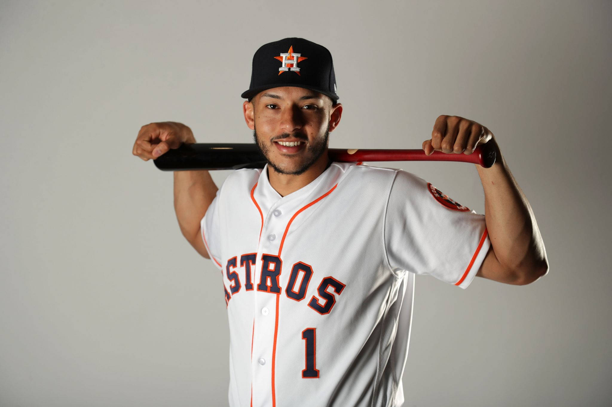 Carlos Correa 桌布 壁紙 — 一位微笑的棒球運動員身穿白色太空人隊球衣，在純灰色工作室背景前將紅色球棒扛在肩上。