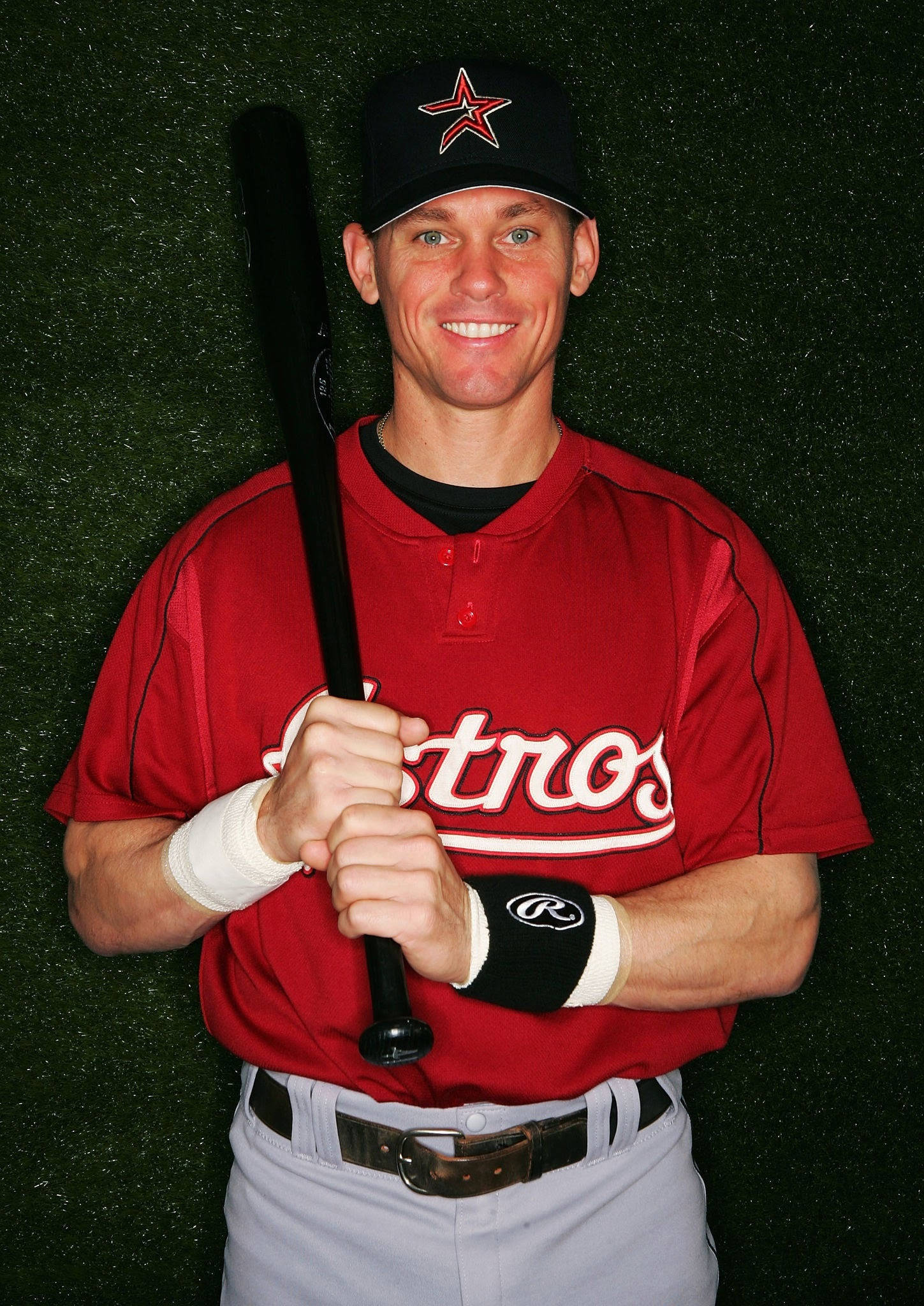 Craig Biggio 桌布 壁紙 — 一位微笑的棒球運動員身穿紅色太空人球衣，在綠色草地背景下手持黑色球棒。