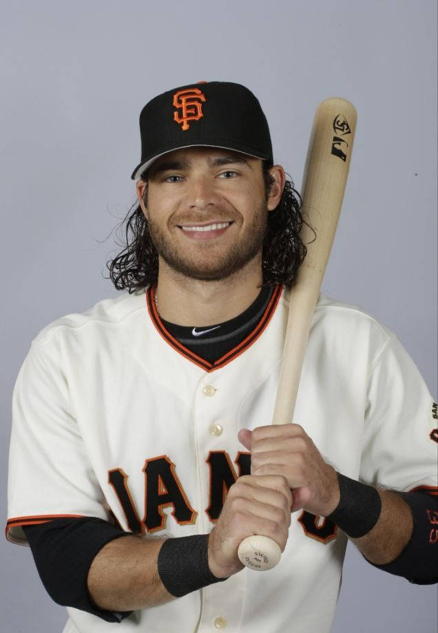 San Francisco Giants 桌布 壁紙 — 一位微笑的棒球運動員身穿舊金山巨人隊制服，在純灰色背景前手持球棒。