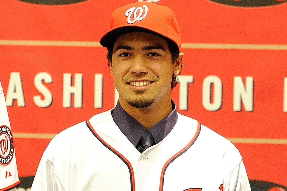 anthony rendon 桌布 壁紙 — 一位微笑的棒球運動員身穿華盛頓國民隊制服，在紅色球隊背景下自信地擺姿勢。