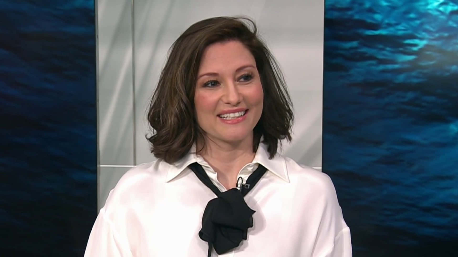 Chyler Leigh 桌布 壁紙 — 一位微笑的棕髮女性，穿著白色襯衫搭配黑色蝴蝶結，背景是藍色水主題。