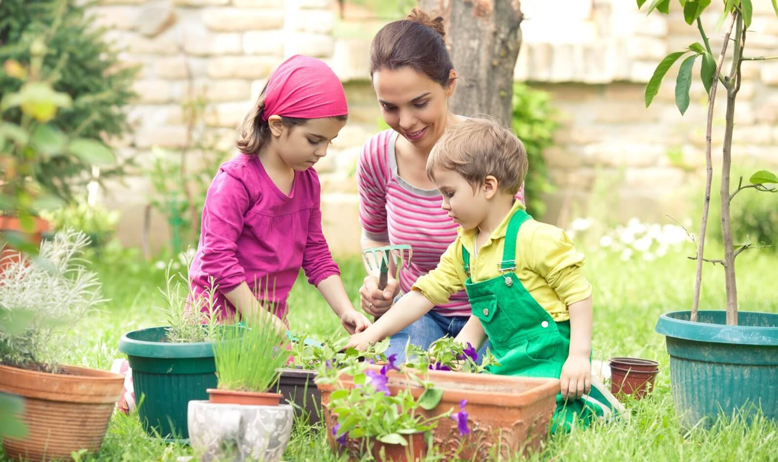 Gardening 桌布 壁紙 — 一位微笑的母親和她的兩個孩子在陽光普照的後院花園照料盆栽植物。