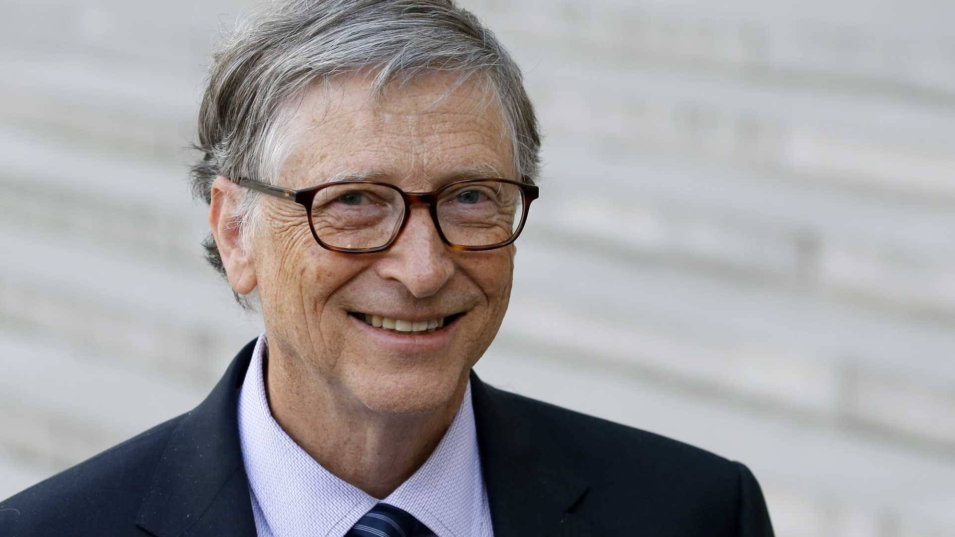gates 桌布 壁紙 — 一位微笑的灰髮戴眼鏡老年男士穿著深色西裝，以模糊的白色磚牆為背景的特寫肖像。
