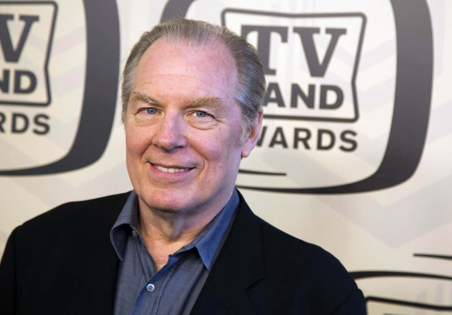 Michael Mckean 桌布 壁紙 — 一位微笑的灰髮藍眼年長男士，在TV Land Awards背景前擺姿勢，身穿黑色西裝外套內搭藍色襯衫。