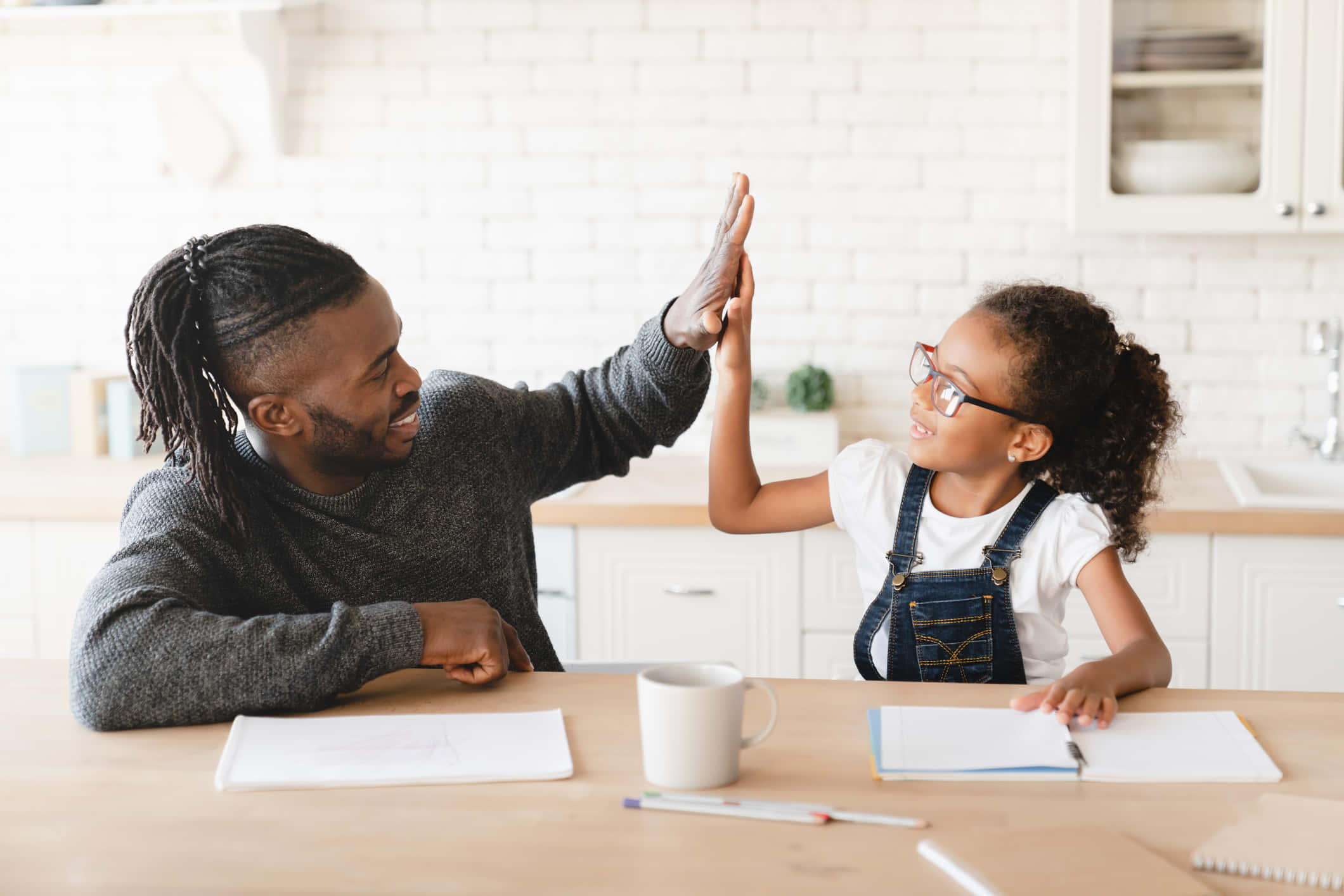 Father 桌布 壁紙 — 一位微笑的父親和女兒在做功課時間於廚房餐桌上擊掌。