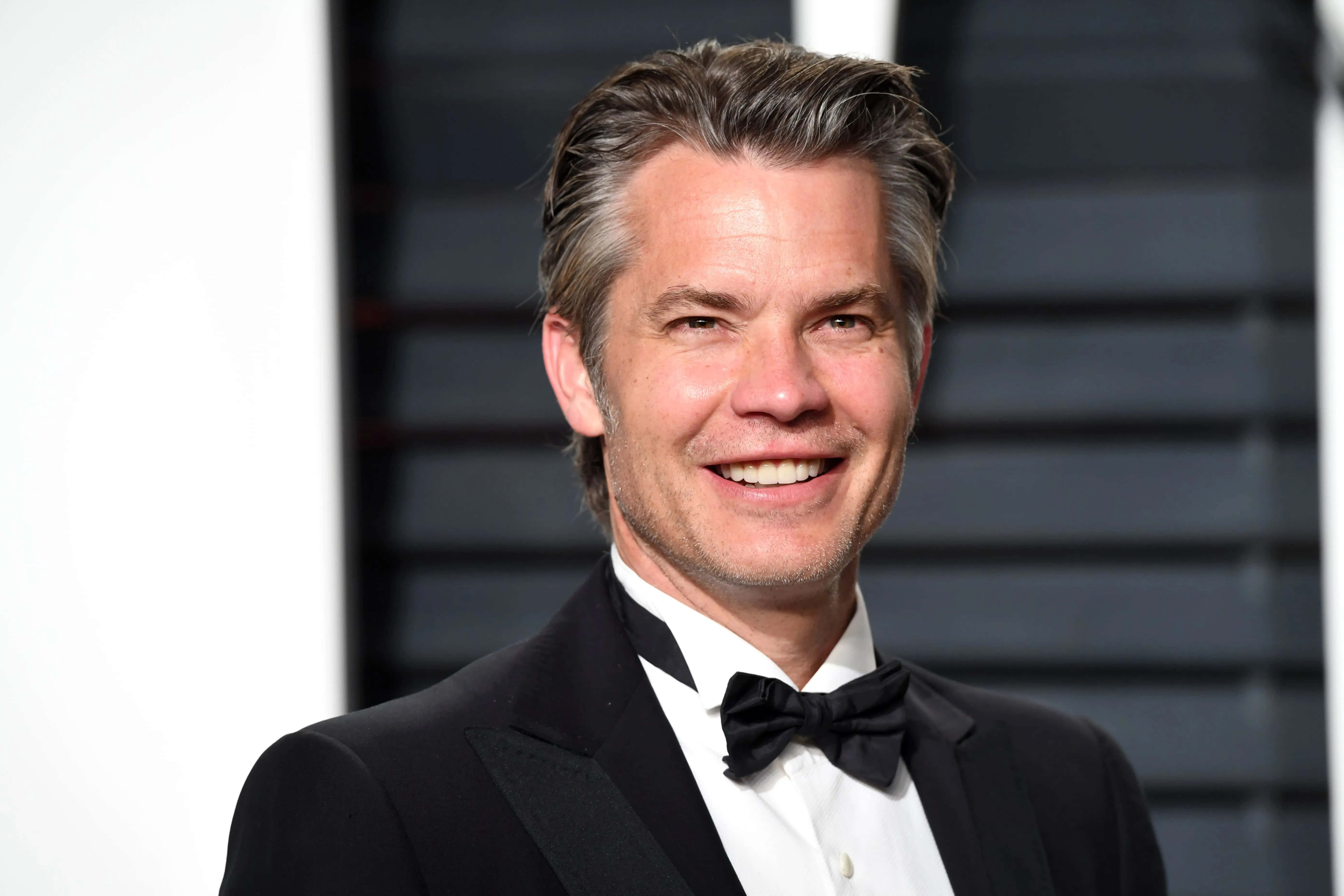 timothy olyphant 桌布 壁紙 — 一位微笑的男人，身穿黑色禮服和蝴蝶結，在深色條紋背景前擺姿勢。