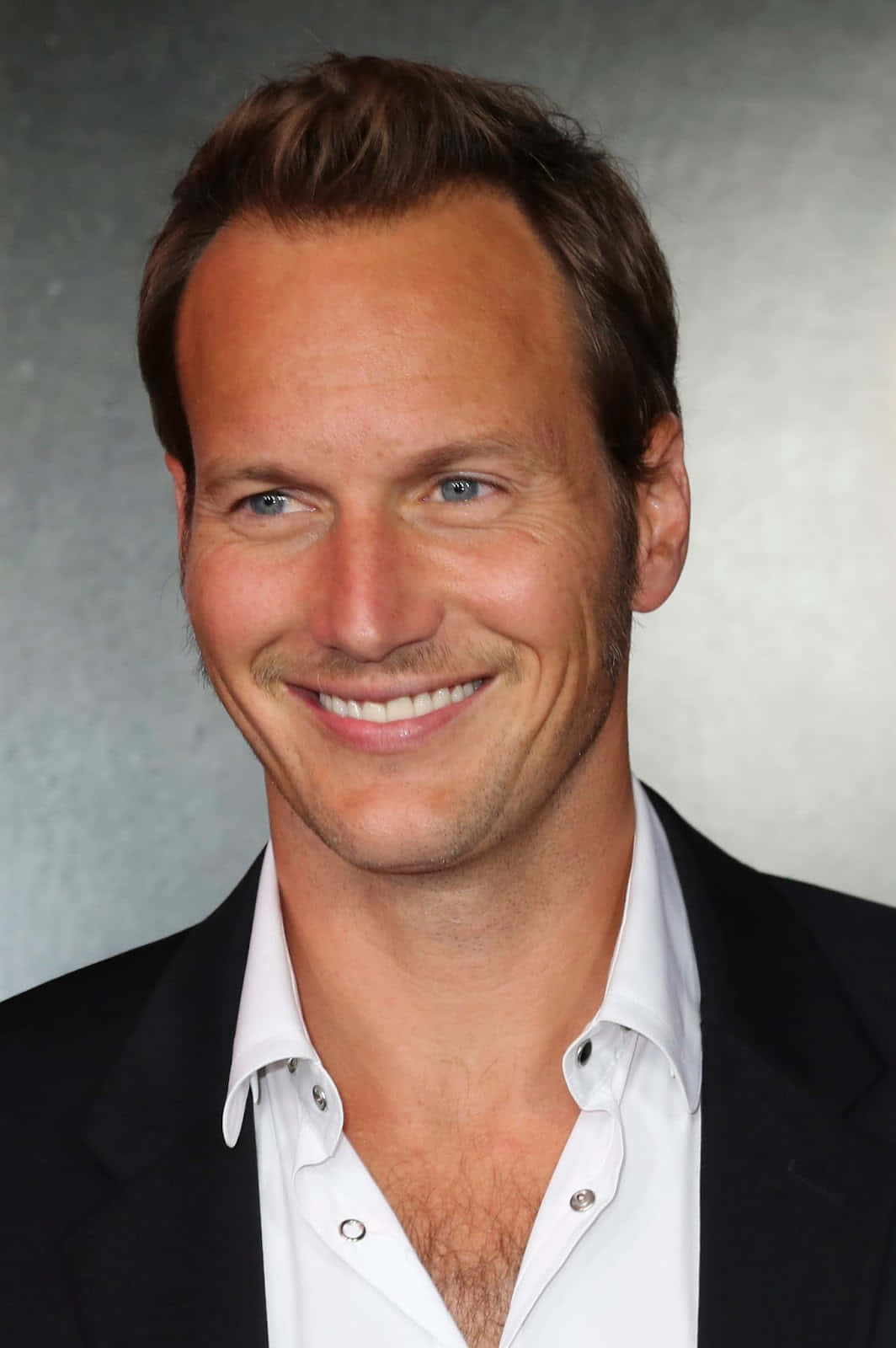 Patrick Wilson 桌布 壁紙 — 一位微笑的男士，藍眼睛，棕色頭髮，穿著黑色西裝外套內搭白色襯衫，背景是灰色攝影棚。