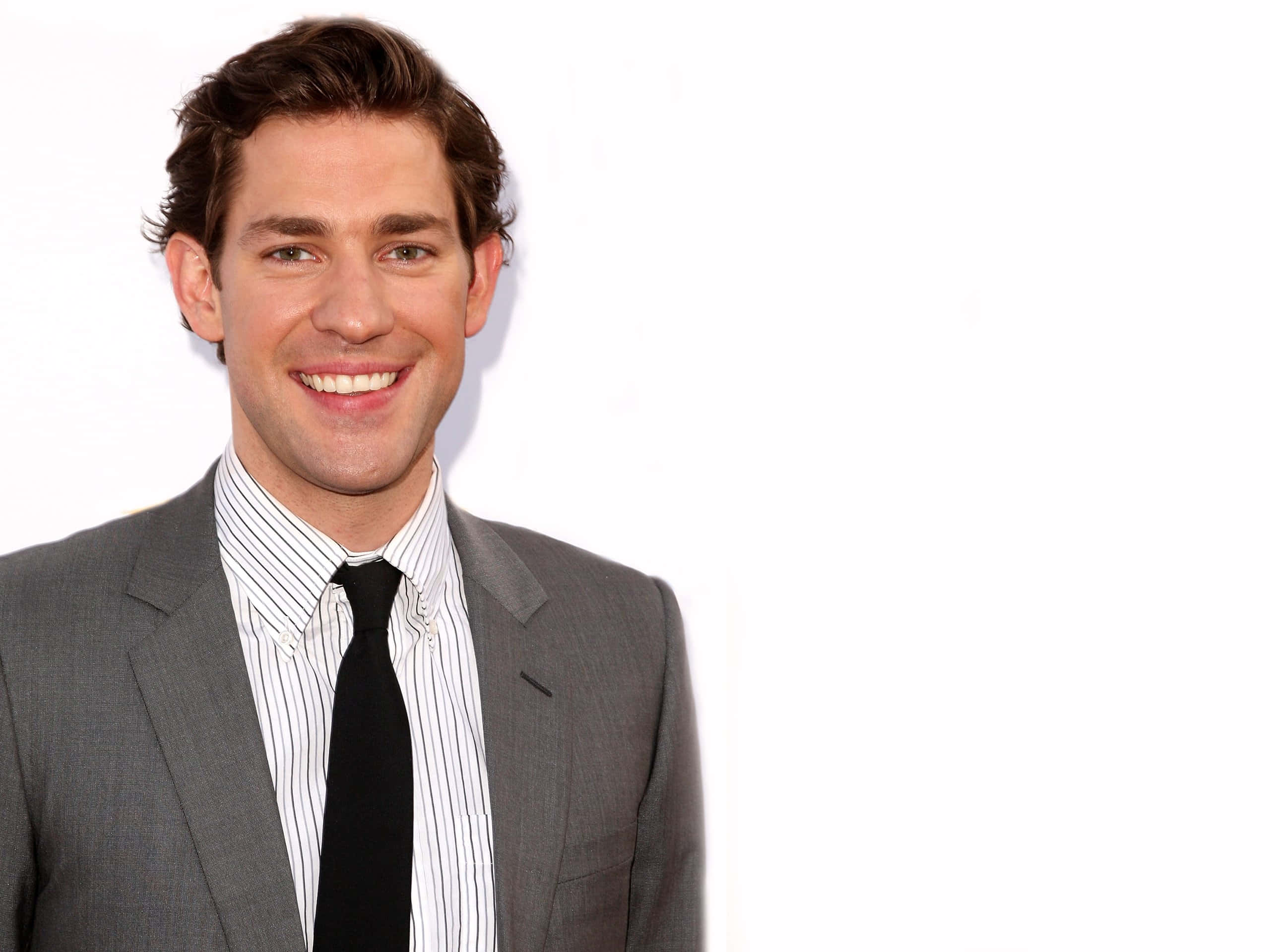 john krasinski 桌布 壁紙 — 一位微笑的男士，身穿灰色西裝和條紋襯衫，在純白色背景前擺姿勢。