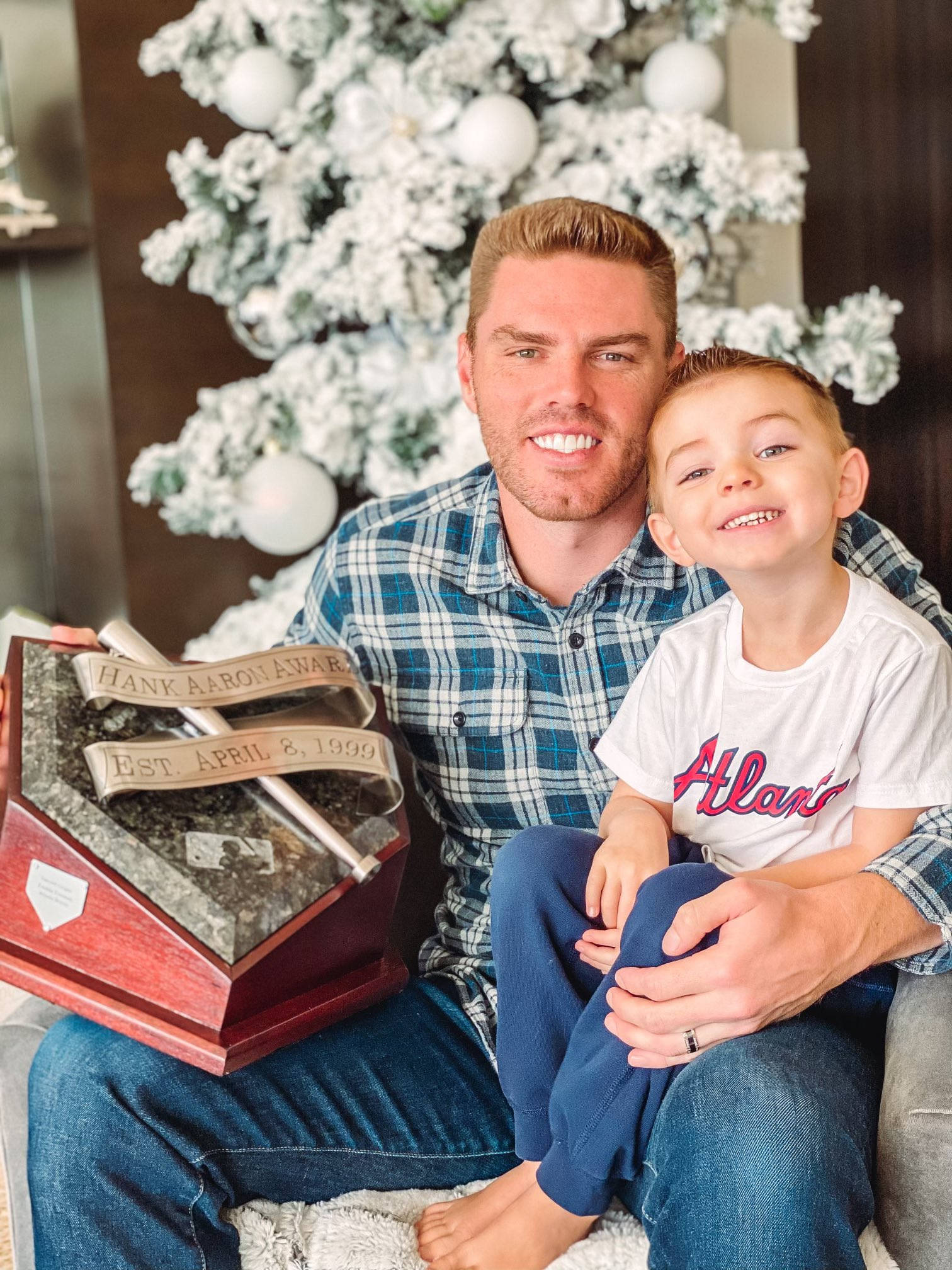 Freddie Freeman 桌布 壁紙 — 一位微笑的男士和一個小男孩一起坐在室內，在白色裝飾樹前拿著漢克·阿倫獎獎盃。