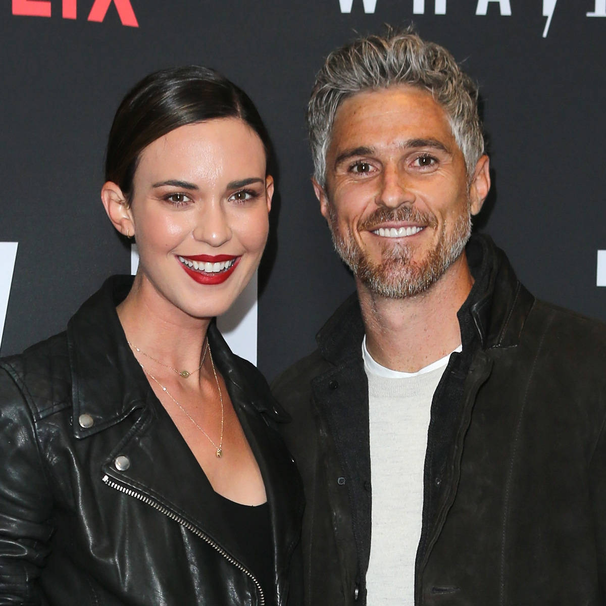 Celebrity 桌布 壁紙 — 一位微笑的男士和女士穿著黑色外套，在Netflix活動中一起擺姿勢，背後有醒目的紅白品牌標誌。