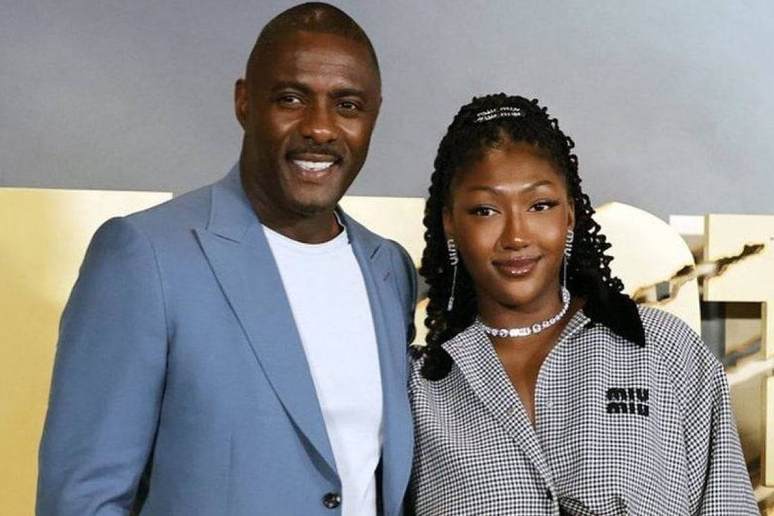 idris elba 桌布 壁紙 — 一位微笑的男士穿著藍色西裝外套，一位女士穿著格紋襯衫，在金色和灰色背景前一起擺姿勢。