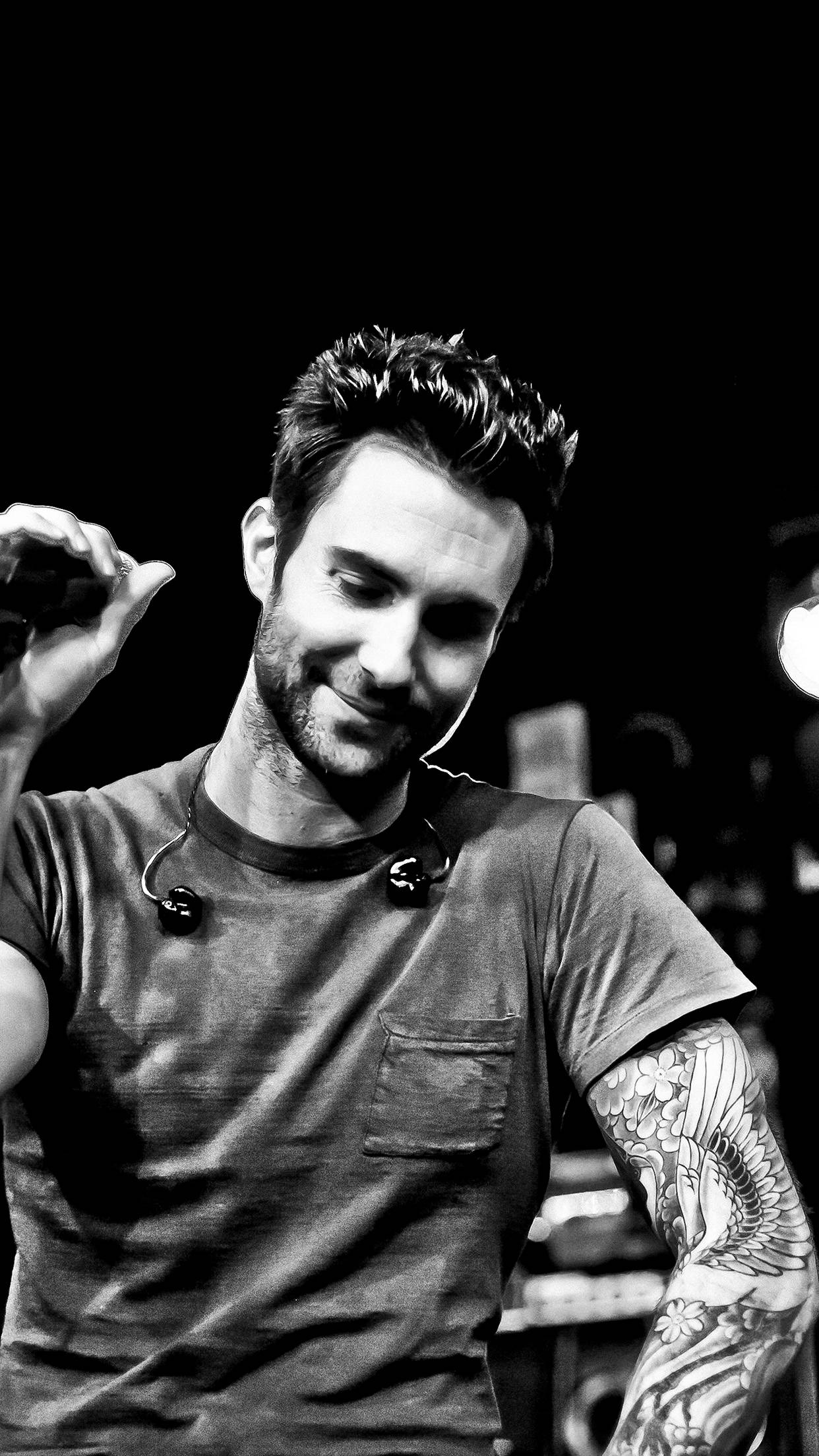 Adam Levine 桌布 壁紙 — 一位微笑的男子，手臂上有刺青並戴著耳機，在深色背景前手持麥克風微笑。