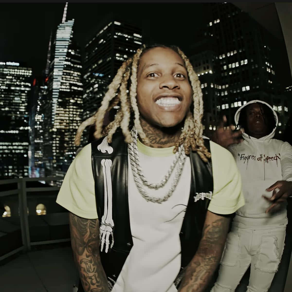 Lil Durk 桌布 壁紙 — 一位微笑的男子，編著辮子頭髮並有刺青，在夜晚的屋頂上以燈火通明的城市天際線為背景擺姿勢。
