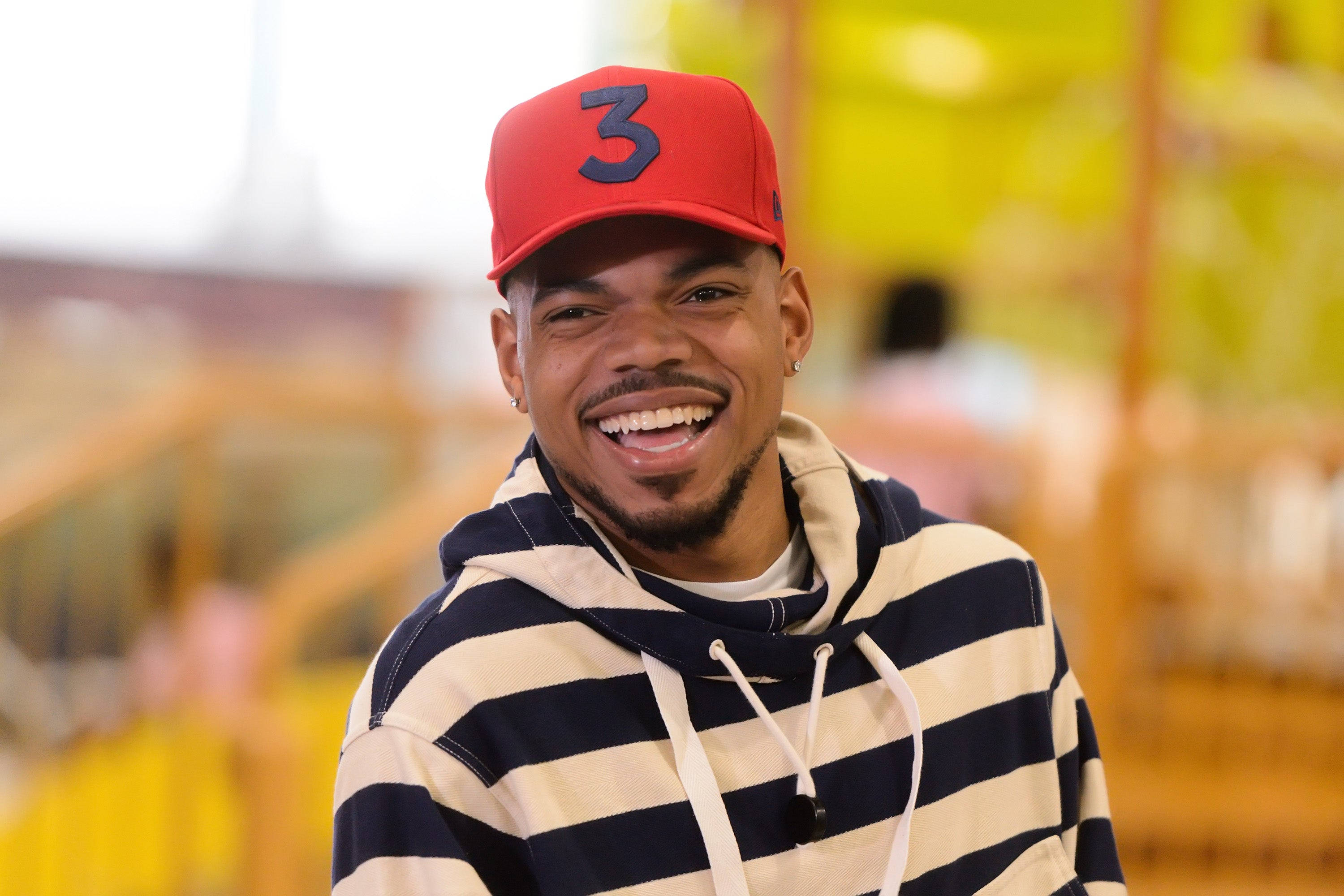 chance 桌布 壁紙 — 一位微笑的男子戴著紅色帽子，上面有黑色數字三，身穿條紋連帽衫，在模糊多彩的背景前開懷大笑。