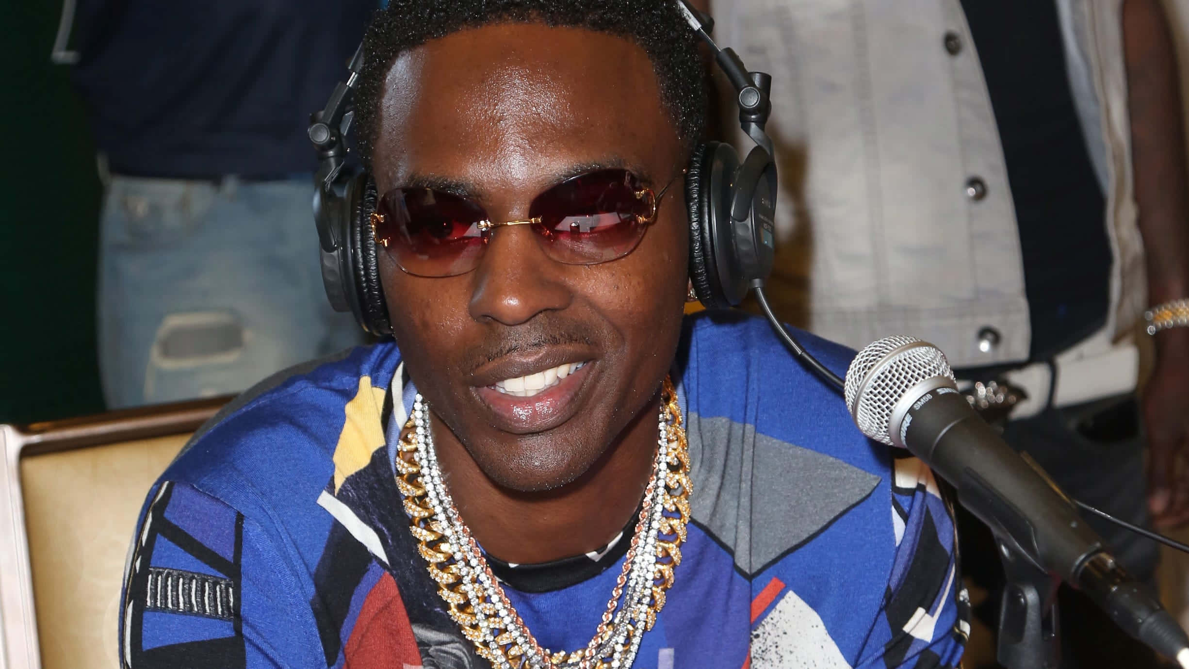 Young Dolph 桌布 壁紙 — 一位微笑的男子戴著耳機和紅色太陽眼鏡，坐在錄音室的麥克風前。