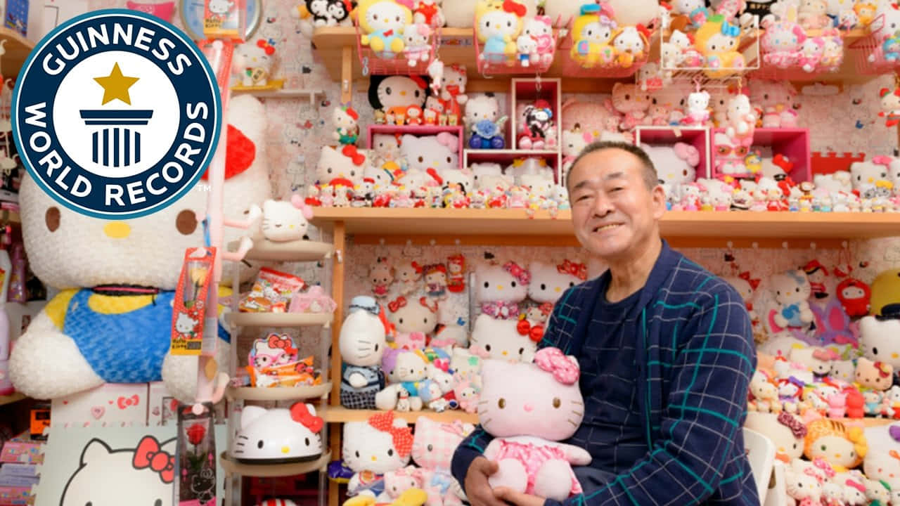 Hello Kitty 桌布 壁紙 — 一位微笑的男子抱著Hello Kitty絨毛玩具，周圍是擺滿色彩繽紛Hello Kitty商品的架子，這是一個金氏世界紀錄認證的收藏。