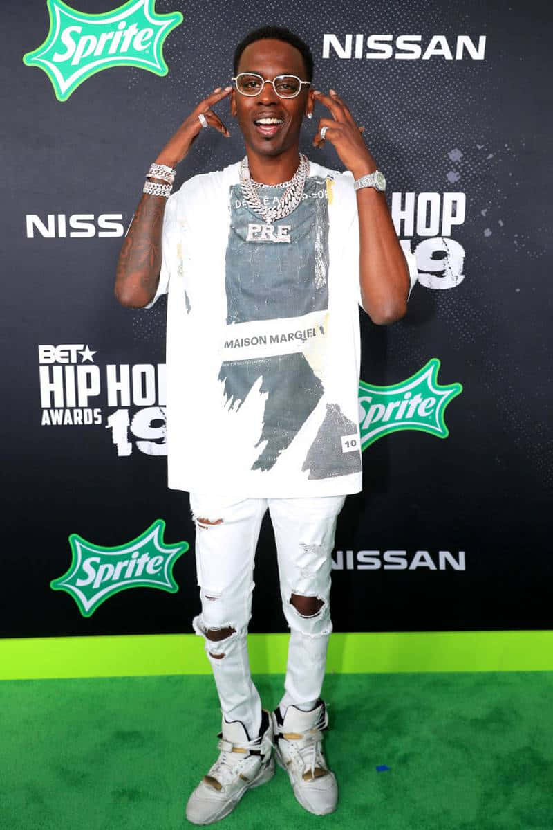 Young Dolph 桌布 壁紙 — 一位微笑的男子穿著白色破洞牛仔褲和眼鏡，在BET Hip Hop Awards的綠色地毯上擺姿勢，身後有Sprite和Nissan的標誌。