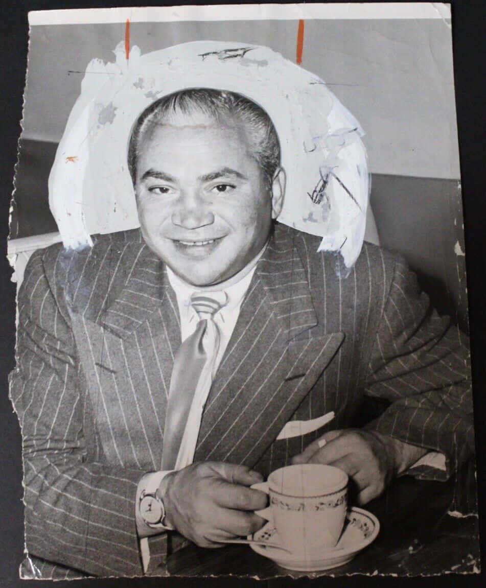 icon 桌布 壁紙 — 一位微笑的男子穿著細條紋西裝，坐在一個損壞的白色紙剪影下方，手持一個茶杯。