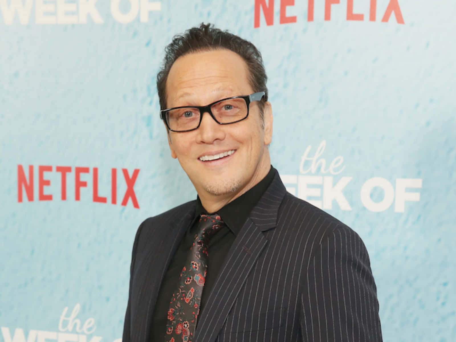 actor 桌布 壁紙 — 一位微笑的男子穿著細條紋西裝和圖案領帶，在淺藍色Netflix活動背景前自信地擺姿勢。