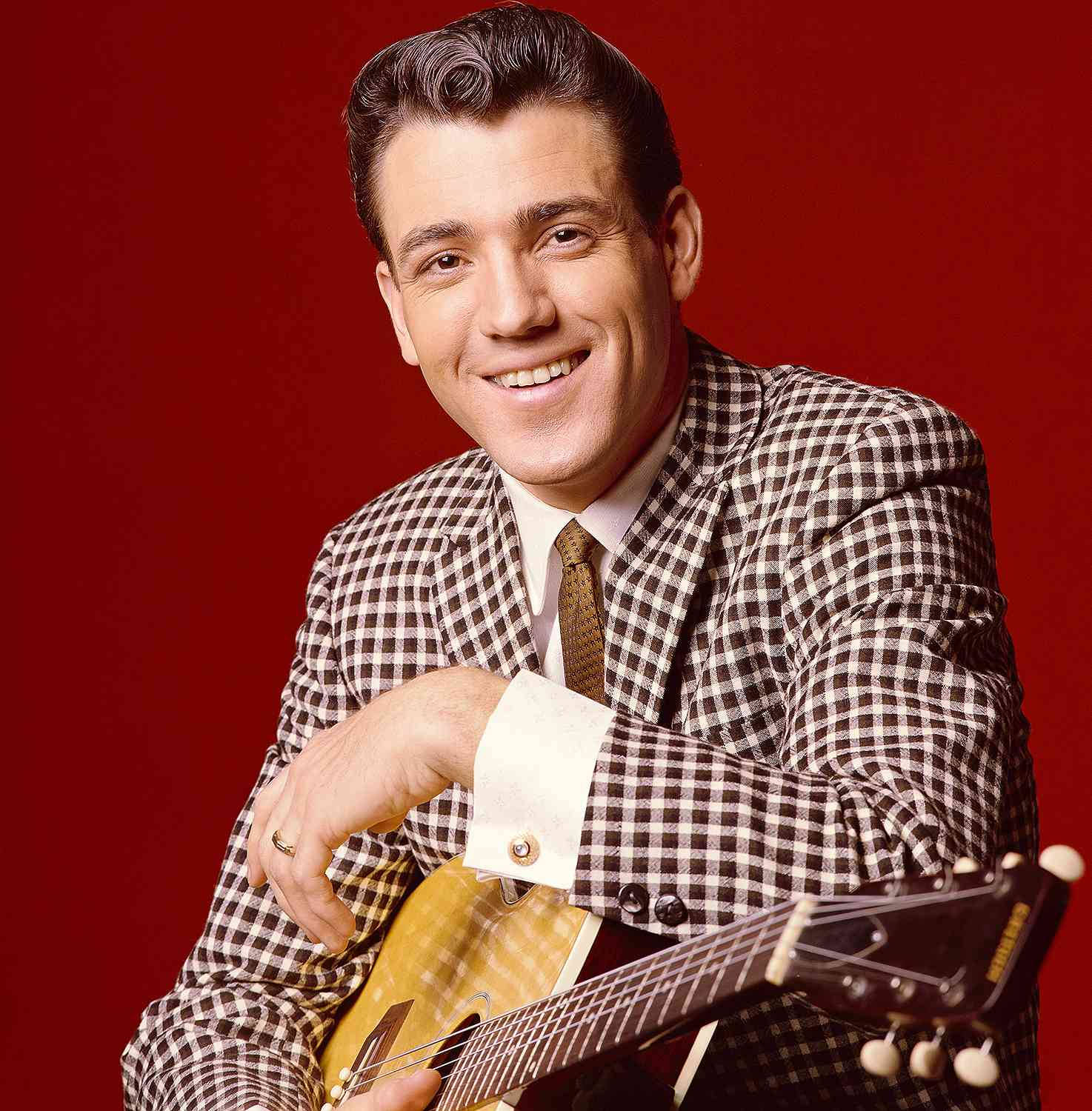 guitar player 桌布 壁紙 — 一位微笑的男子身穿格紋西裝，在復古工作室燈光的鮮明紅色背景前拿著吉他。