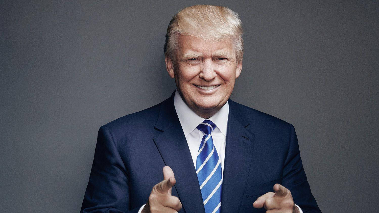 donald trump 桌布 壁紙 — 一位微笑的男子身穿海軍藍西裝和藍色條紋領帶，在純灰色工作室背景前向前做手勢。
