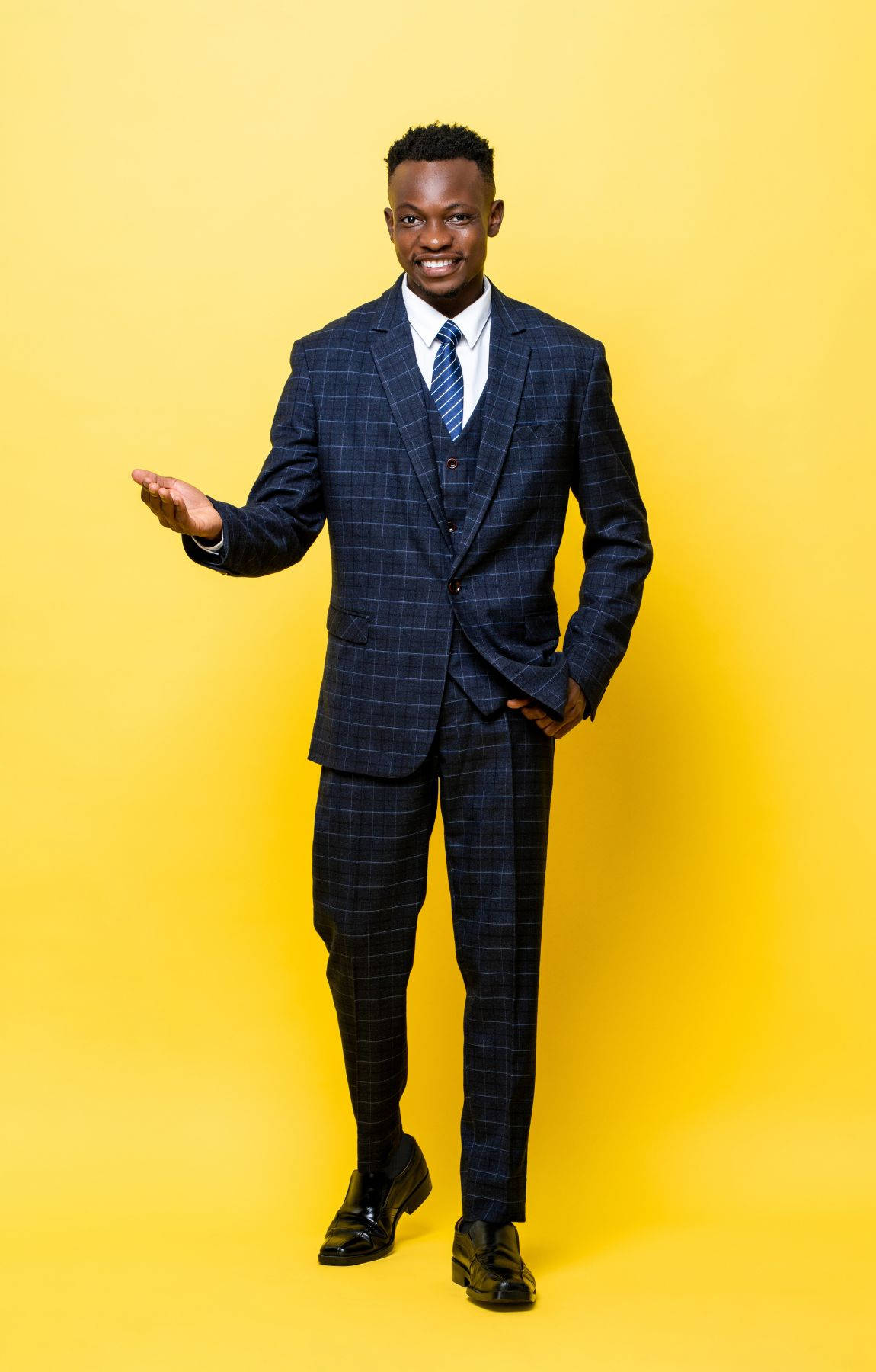 suit 桌布 壁紙 — 一位微笑的男子身穿深色格紋西裝，在鮮黃色的攝影棚背景前熱情地做手勢。