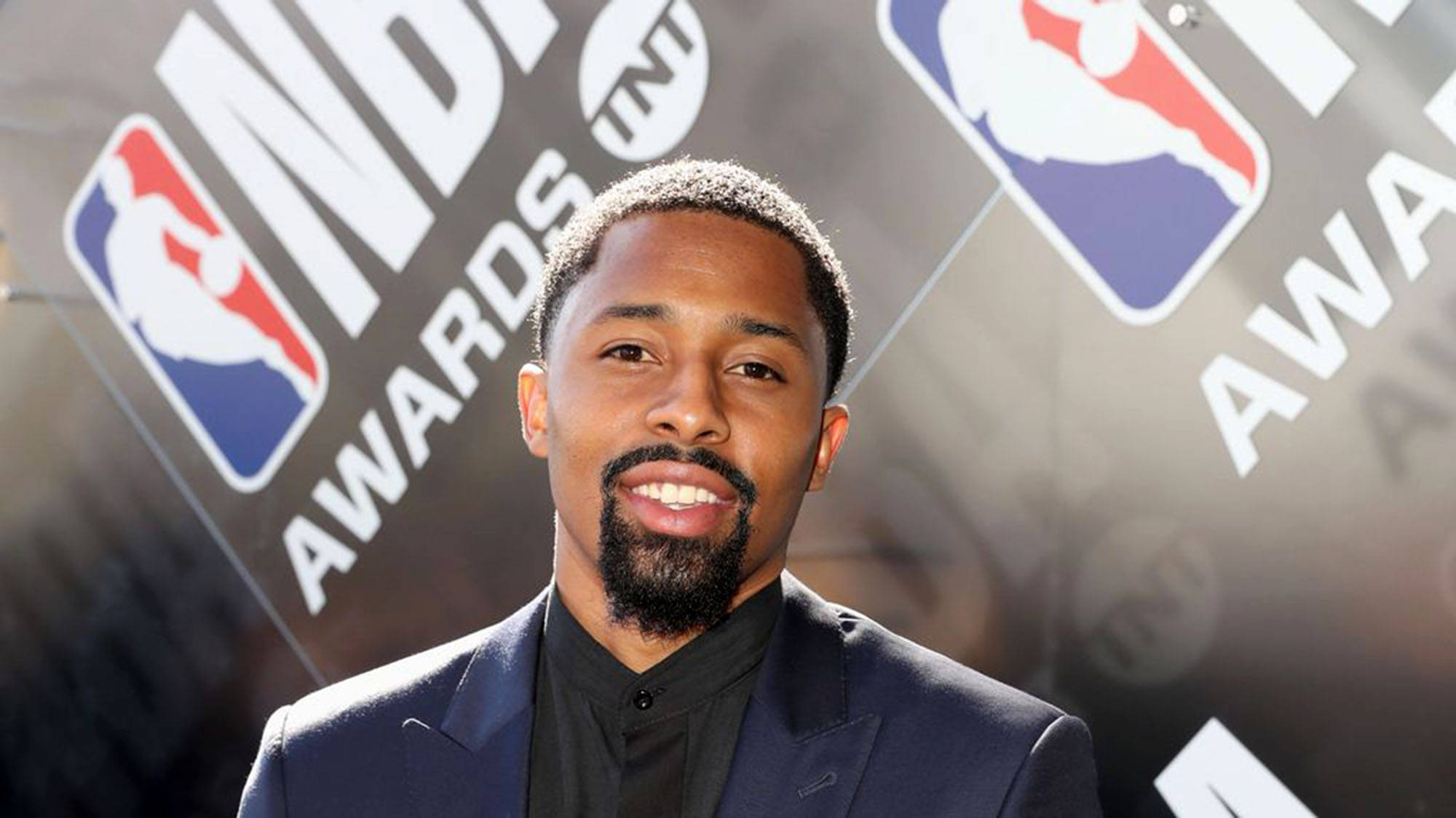 spencer dinwiddie 桌布 壁紙 — 一位微笑的男子身穿深色西裝，站在NBA Awards標誌的背景前，燈光明亮。