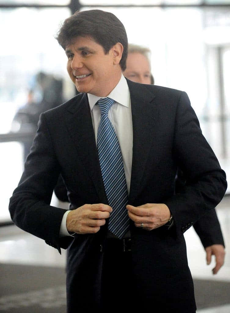 Celebrity 桌布 壁紙 — 一位微笑的男子身穿深色西裝和條紋領帶，在明亮的室內環境中扣上外套的鈕扣。