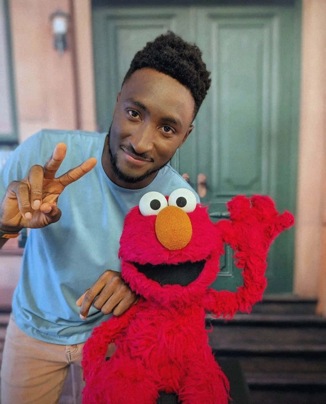 Elmo 桌布 壁紙 — 一位微笑的男子身穿淺藍色襯衫，在綠色門前的門廊階梯上與紅色Elmo公仔合影。