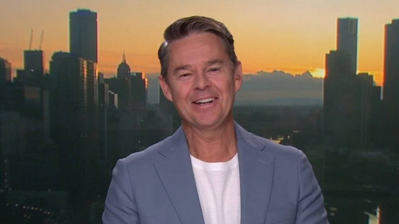 Celebrity 桌布 壁紙 — 一位微笑的男子身穿淺藍色西裝外套，站在充滿活力的日落城市景觀前，高樓大廈林立。