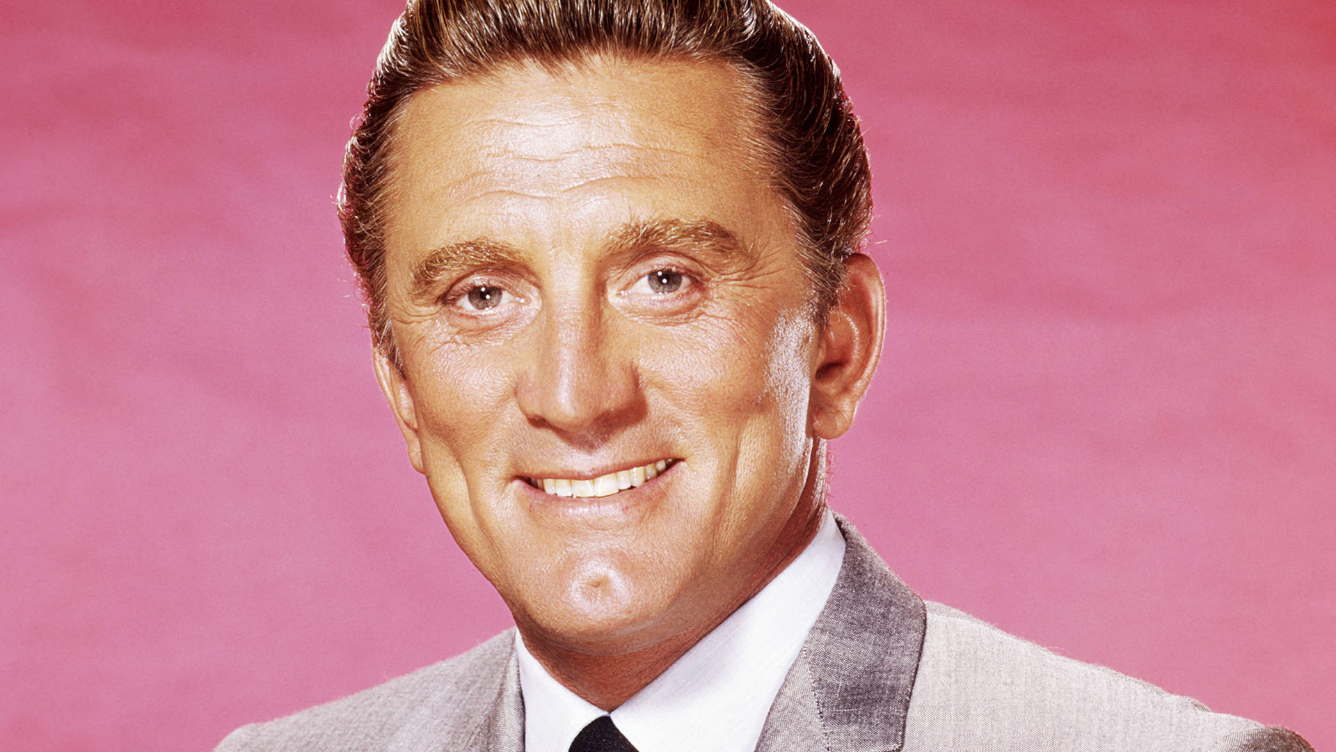 actor 桌布 壁紙 — 一位微笑的男子身穿灰色西裝和黑色領帶，在純粉色攝影棚背景前擺姿勢。