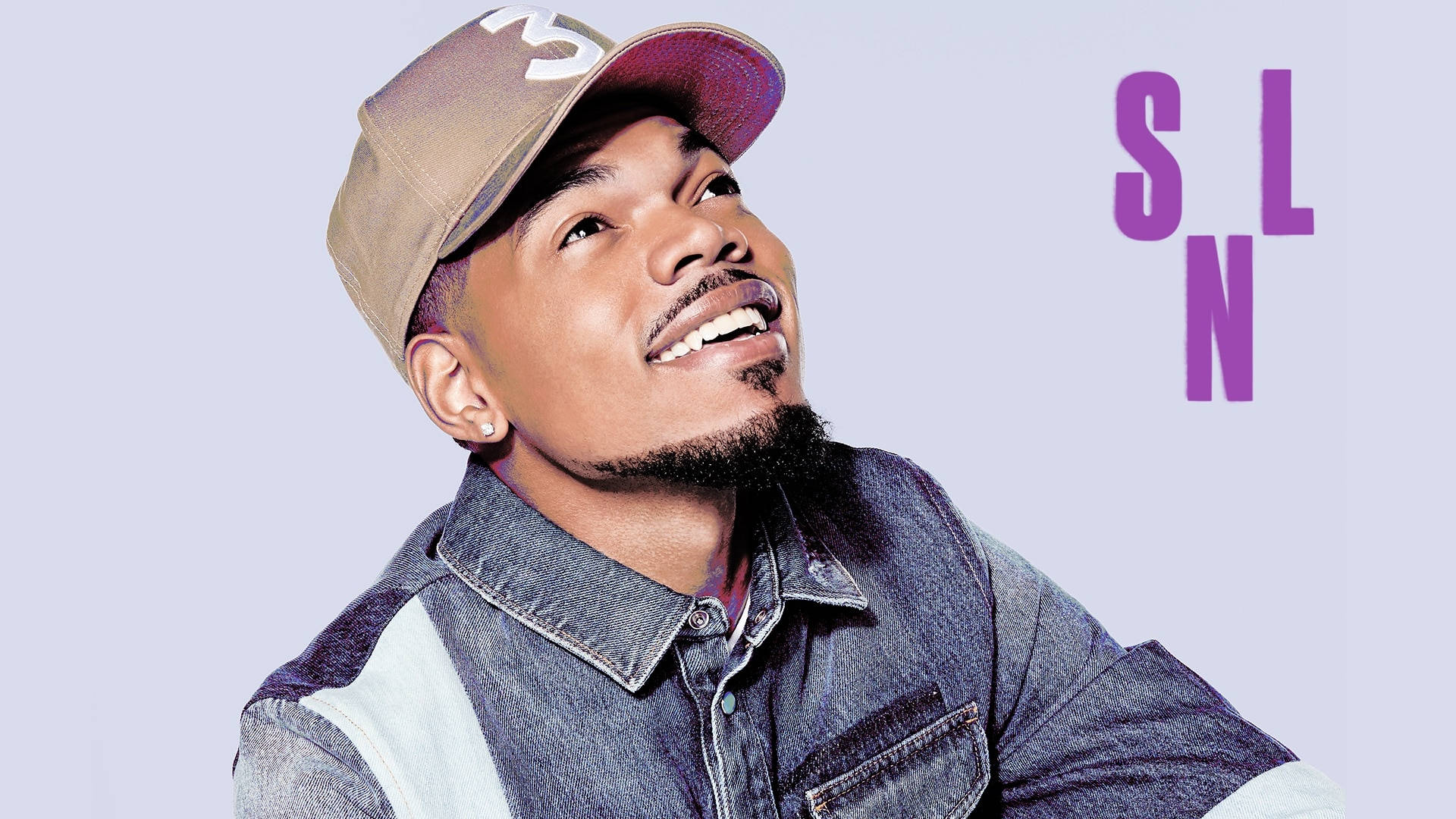 chance 桌布 壁紙 — 一位微笑的男子身穿牛仔外套和帽子，在柔和的薰衣草背景上仰望粗體紫色字母。