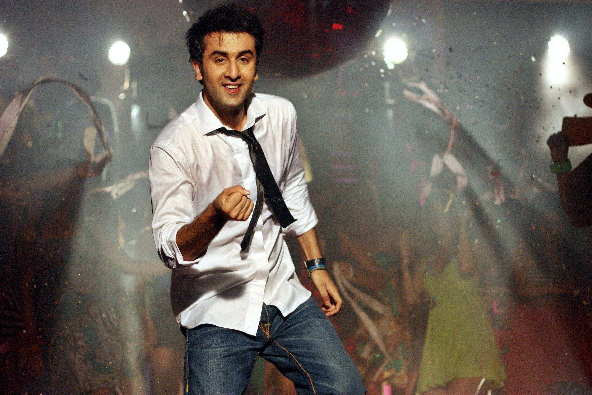 Ranbir Kapoor 桌布 壁紙 — 一位微笑的男子身穿白襯衫、領帶鬆開，在煙霧瀰漫、燈光閃爍、撒滿五彩碎紙的夜店中充滿活力地跳舞。