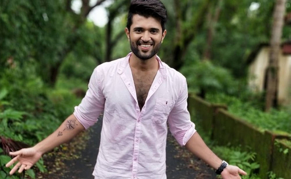 vijay devarakonda 4K 桌布 壁紙 — 一位微笑的男子身穿粉紅色襯衫，在翠綠的森林小徑上張開雙臂。