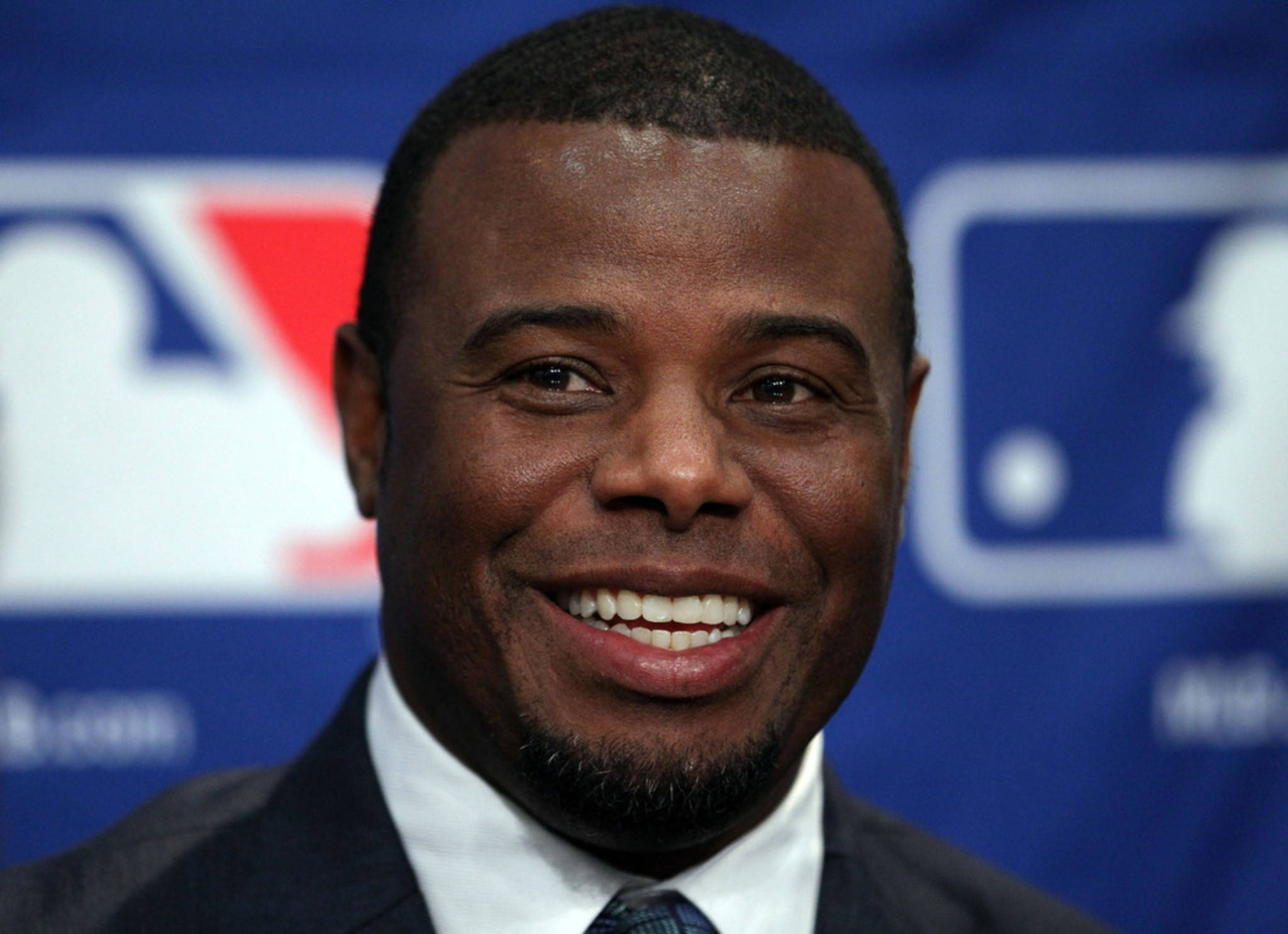 ken 桌布 壁紙 — 一位微笑的男子身穿西裝打領帶，站在帶有標誌的藍色 MLB 背景前。