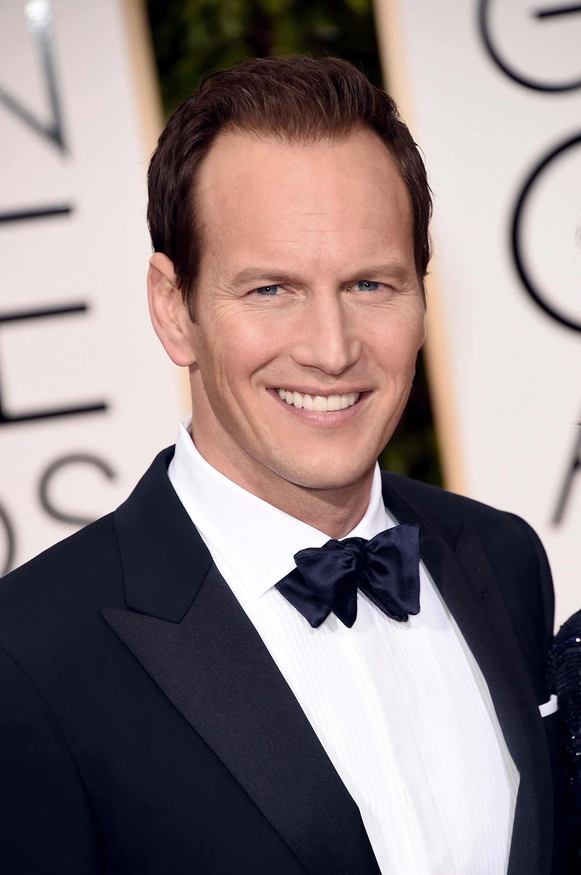 Patrick Wilson 桌布 壁紙 — 一位微笑的男子身穿黑色燕尾服和領結，在身後有金色字體的華麗頒獎活動中擺姿勢。