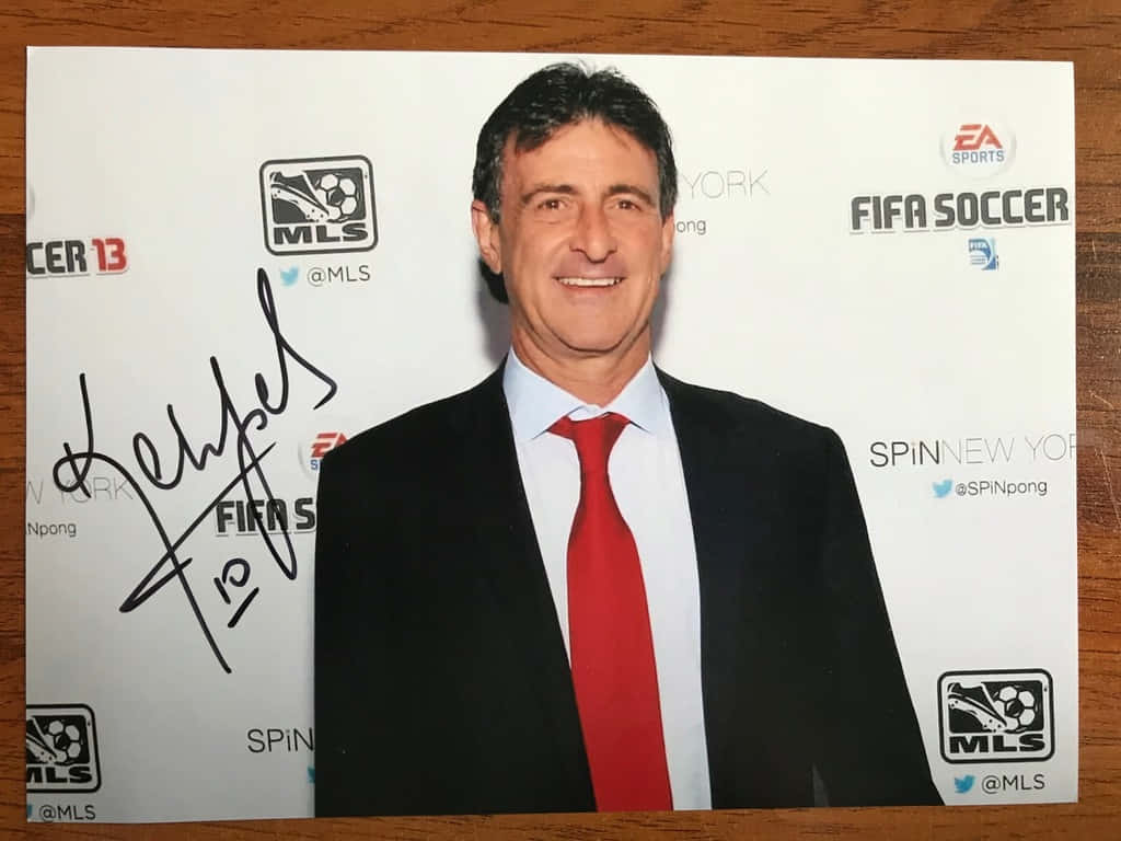 Smile 桌布 壁紙 — 一位微笑的男子身穿黑色西裝和紅色領帶，在FIFA足球活動中擺姿勢，照片上有標誌和他的簽名。