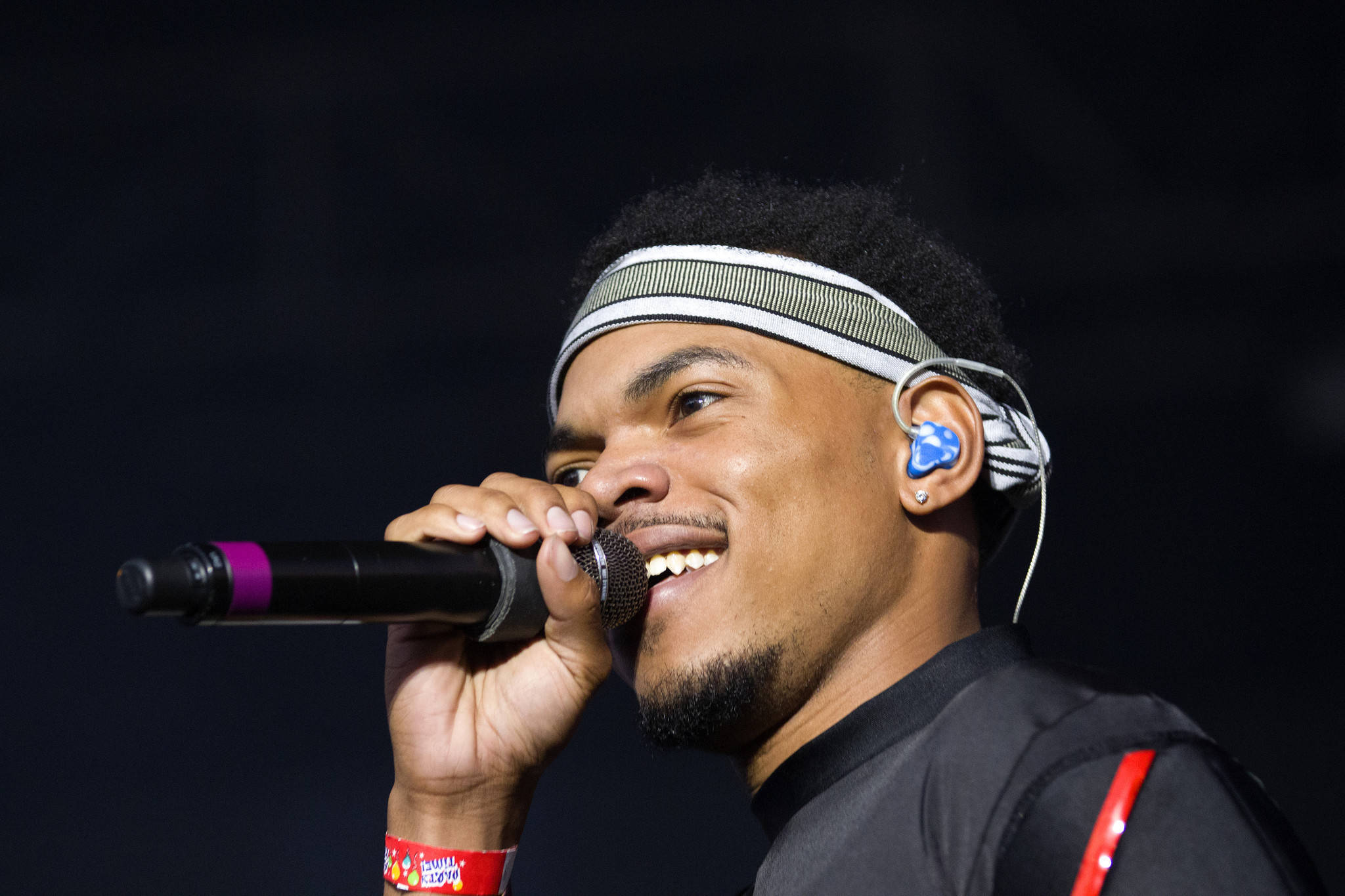 chance 桌布 壁紙 — 一位微笑的男性表演者在舞台燈光下對著麥克風唱歌，背景昏暗。