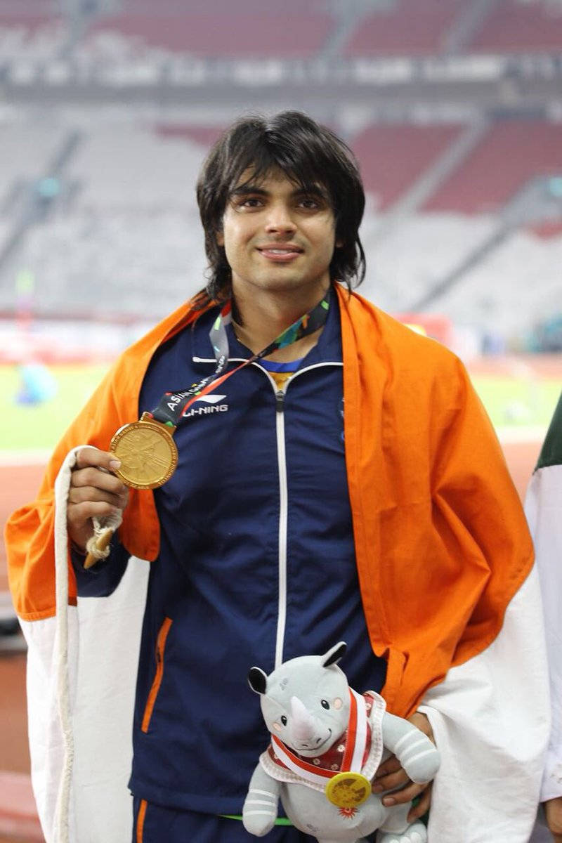 Athletic 桌布 壁紙 — 一位微笑的男性運動員身穿藍色運動服，手持金牌和一個披著橙白旗幟的犀牛絨毛吉祥物。