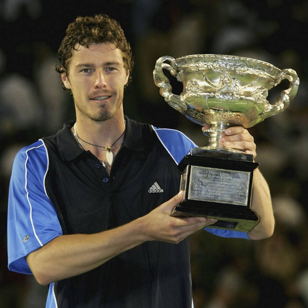 Australian Open 桌布 壁紙 — 一位微笑的男網球選手在體育場燈光下自豪地高舉一個大型華麗銀色獎盃。