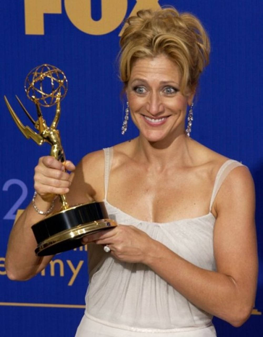Celebrity 桌布 壁紙 — 一位微笑的白裙女士在藍色背景前手持金色艾美獎，背景有 'FOX' 和 'Emmy' 標誌。