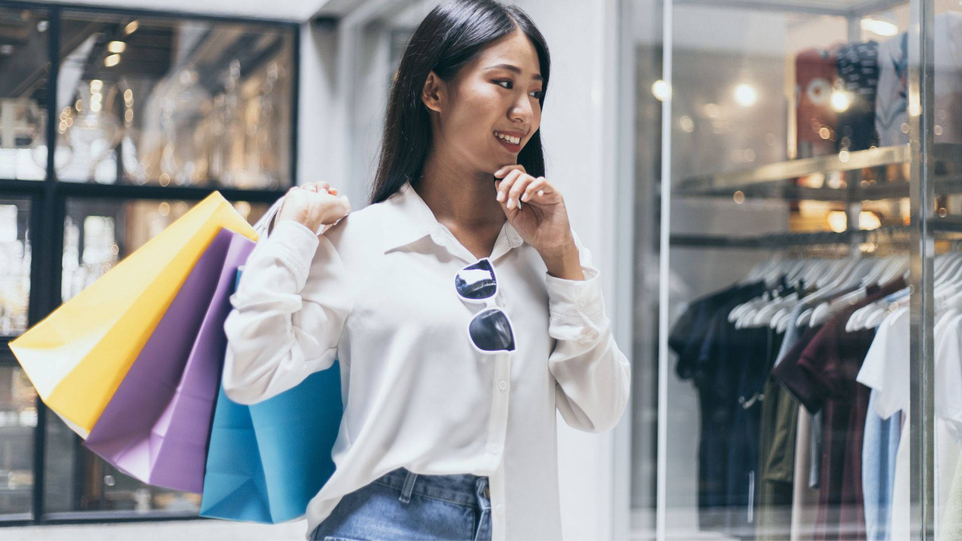 Clothes 桌布 壁紙 — 一位微笑的白襯衫女士拿著色彩繽紛的購物袋，同時看著商店櫥窗裡的衣服。
