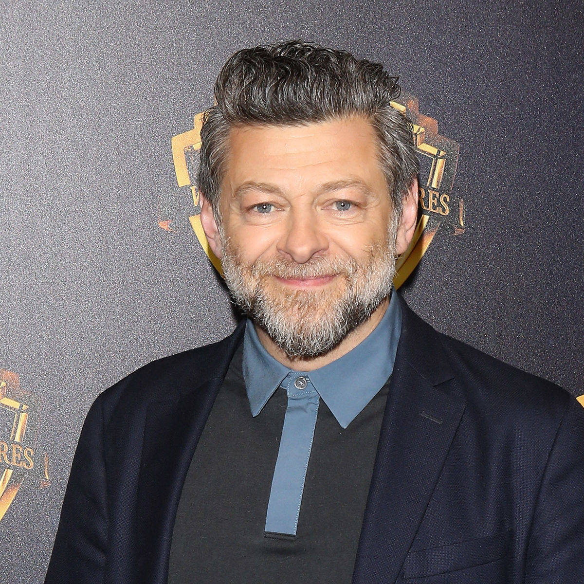 actor 桌布 壁紙 — 一位微笑的白髮灰鬍男子，身穿深色西裝和藍色襯衫，背景為帶有金色標誌的紋理背景。